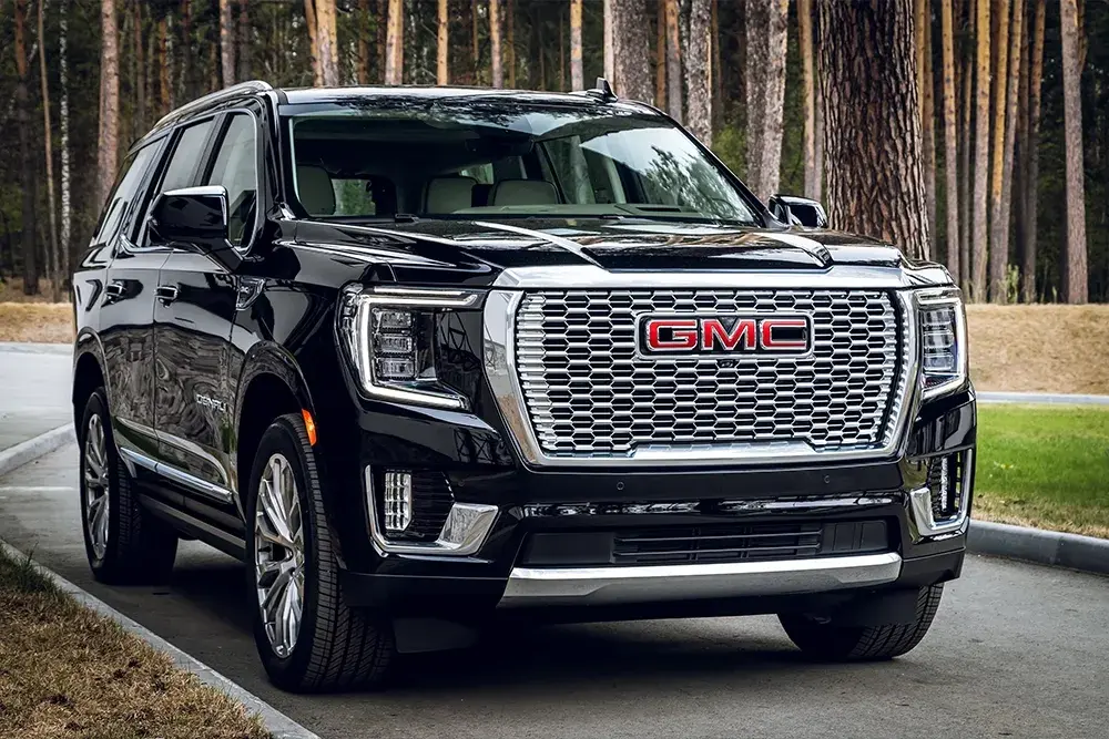 The image shows a black GMC SUV parked on a paved road with trees in the background.